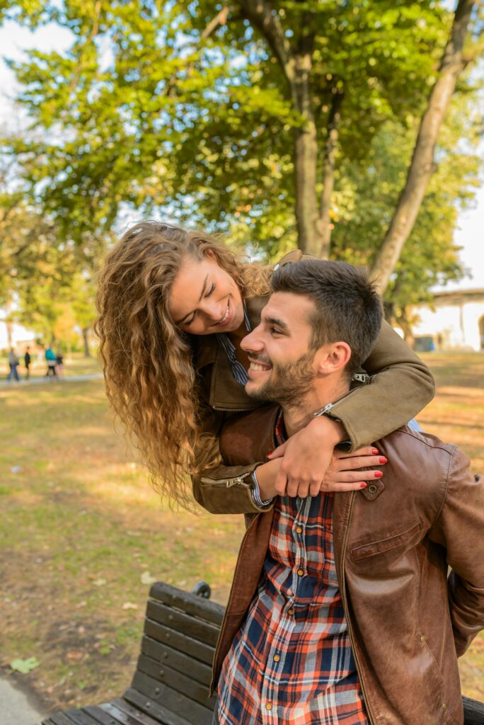 Smiling couple enjoying a playful moment outdoors in a sunny park.